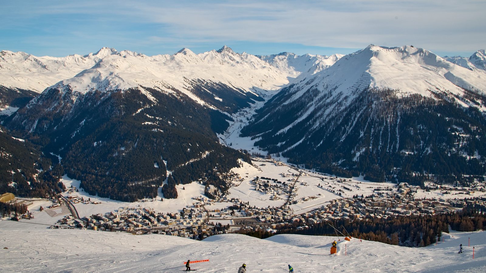 Skiers on an alpine slope above a snowy mountain resort town